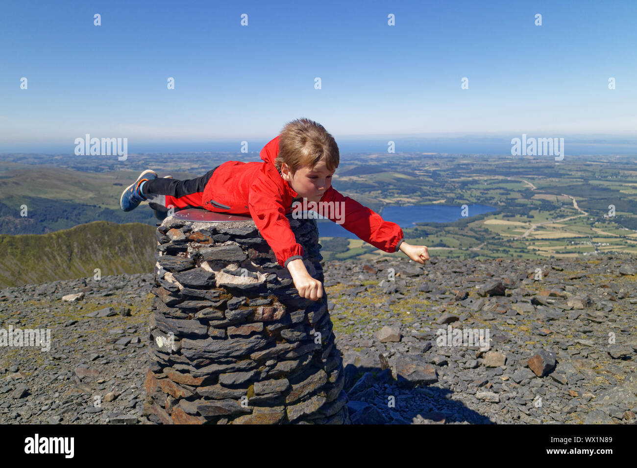 A young boy (7 yrs old) pretending to be Superman on the summit of Skiddaw in the Lake District Stock Photo