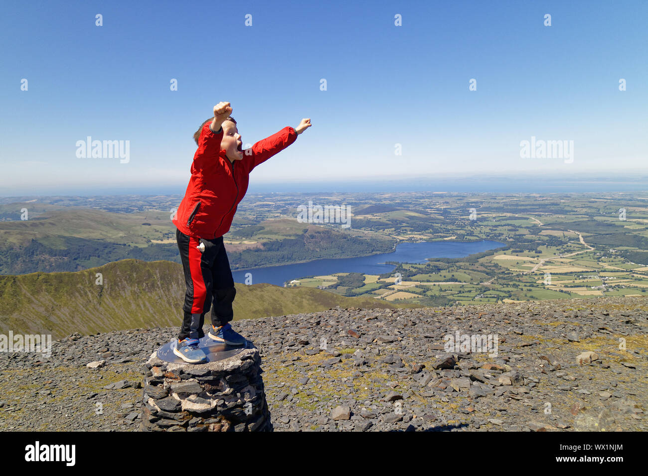A young boy (7 yrs old) celebrates on reaching the summit of Skiddaw, a mountain in the Lake District, Cumbria, UK Stock Photo