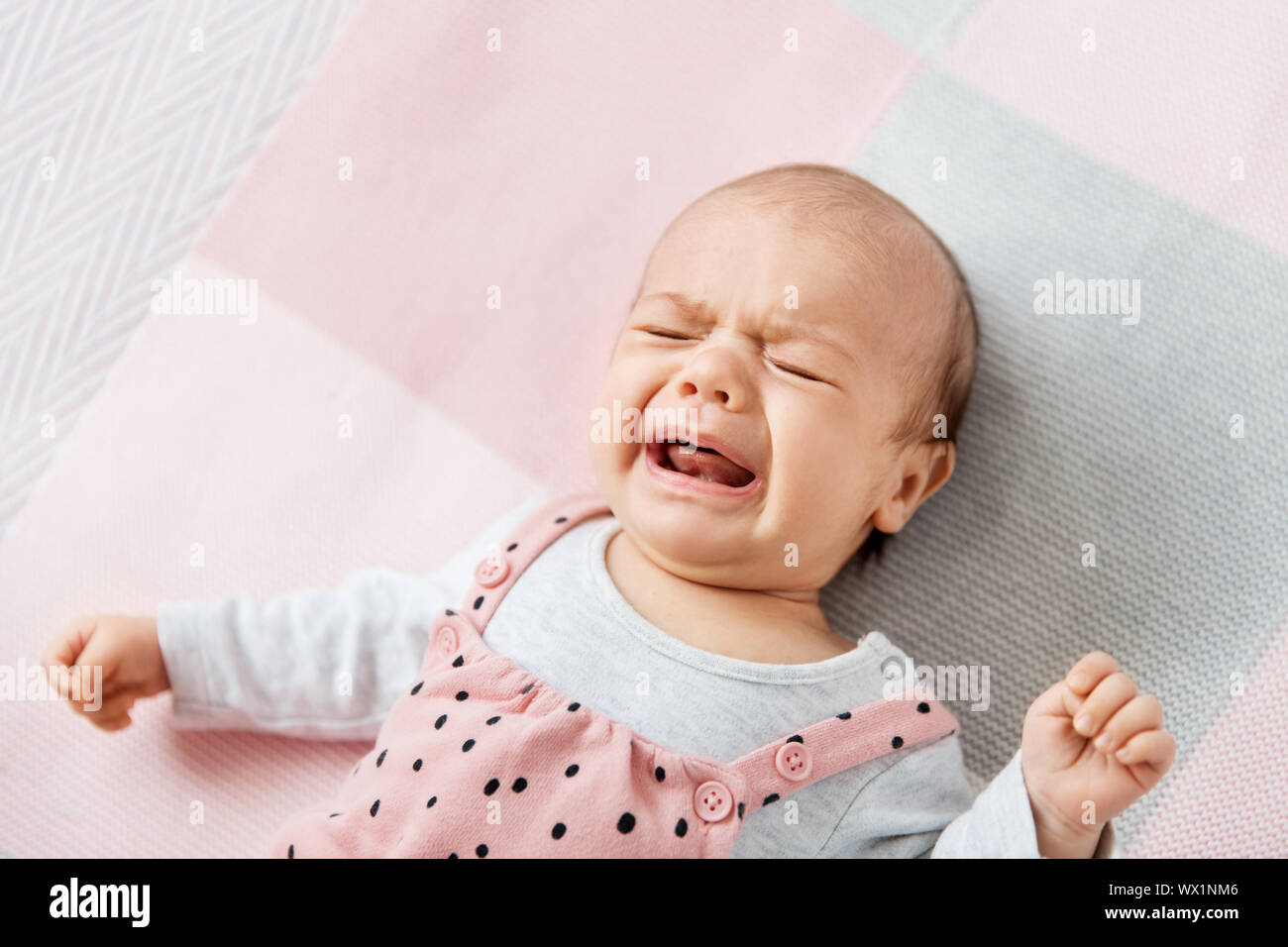 crying baby girl lying on knitted blanket Stock Photo Alamy
