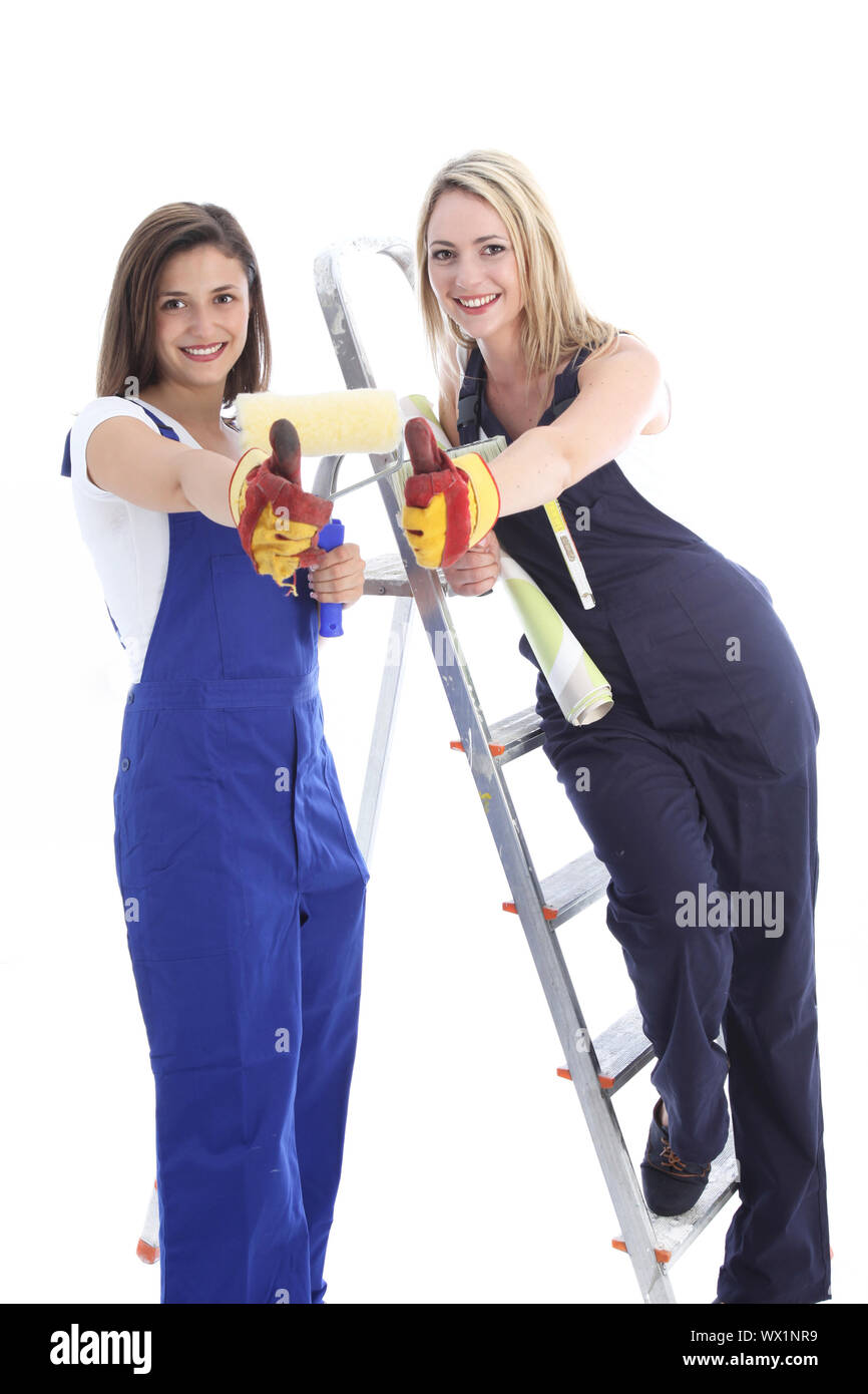 Two happy women dressed in dungarees and safety gloves give a thumbs up ...