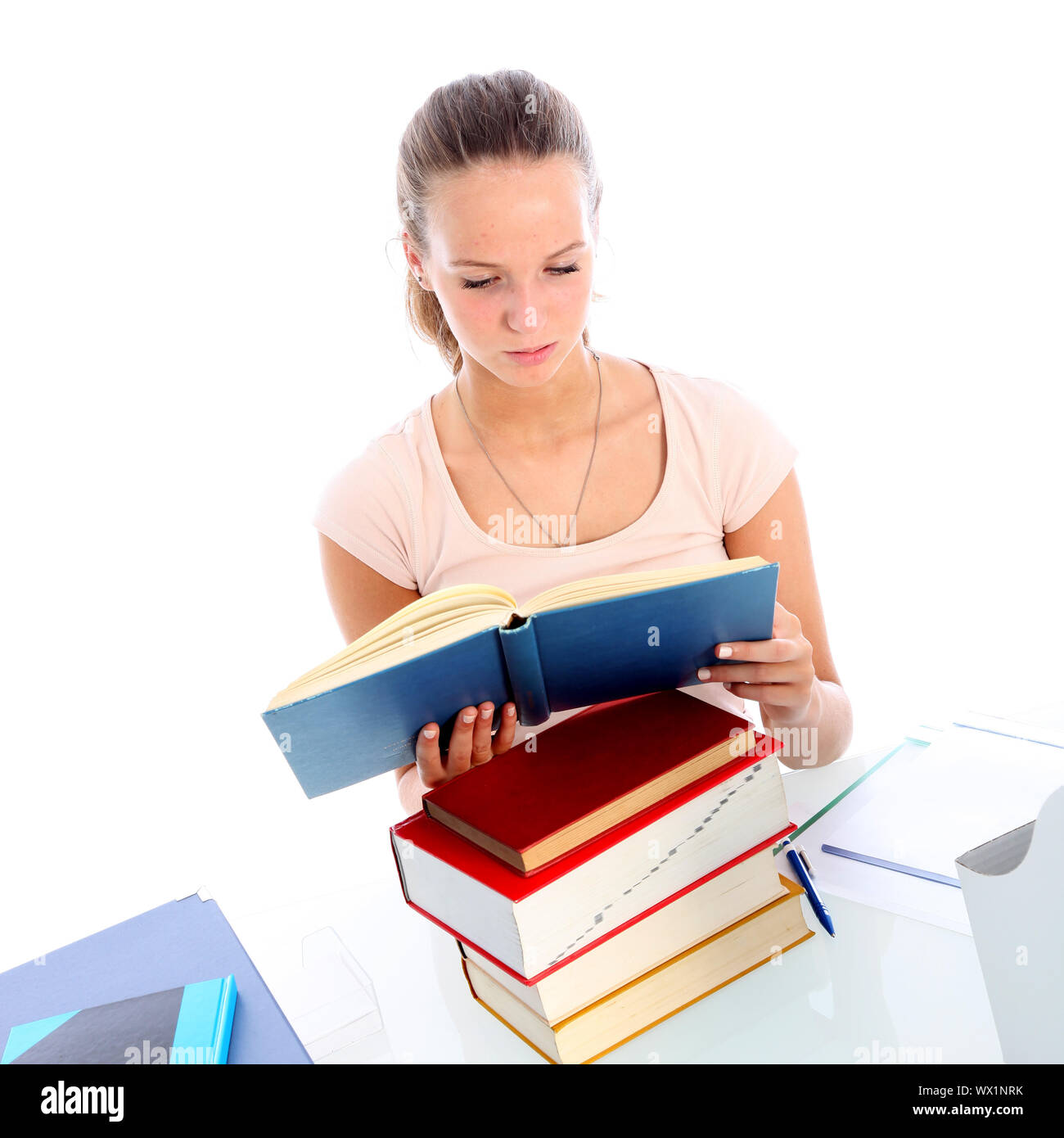 Dedicated young female student sitting at her desk with a pile of books ...