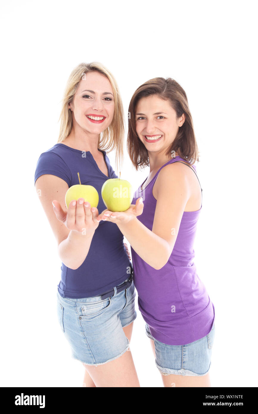 Two happy young women with apples balanced on their open palms standing facing each other in casual denim shorts Stock Photo