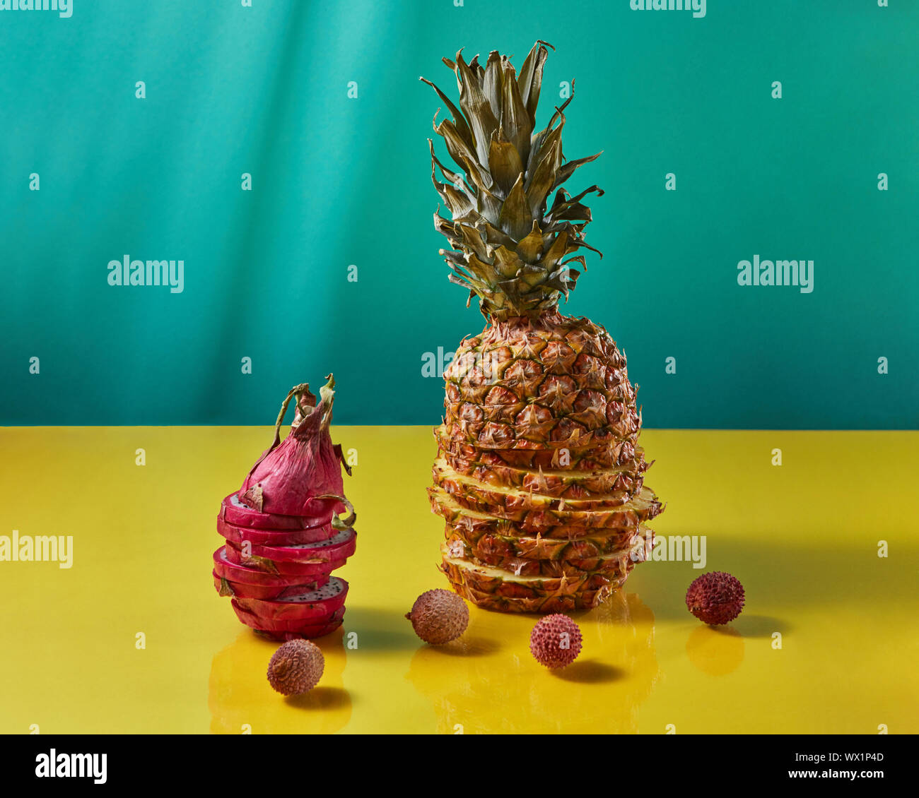Tropical Pineapple fruit single whole and dragon fruit, pitaya made up of sliceson and litchi fruits on a duotone yellow-blue ba Stock Photo