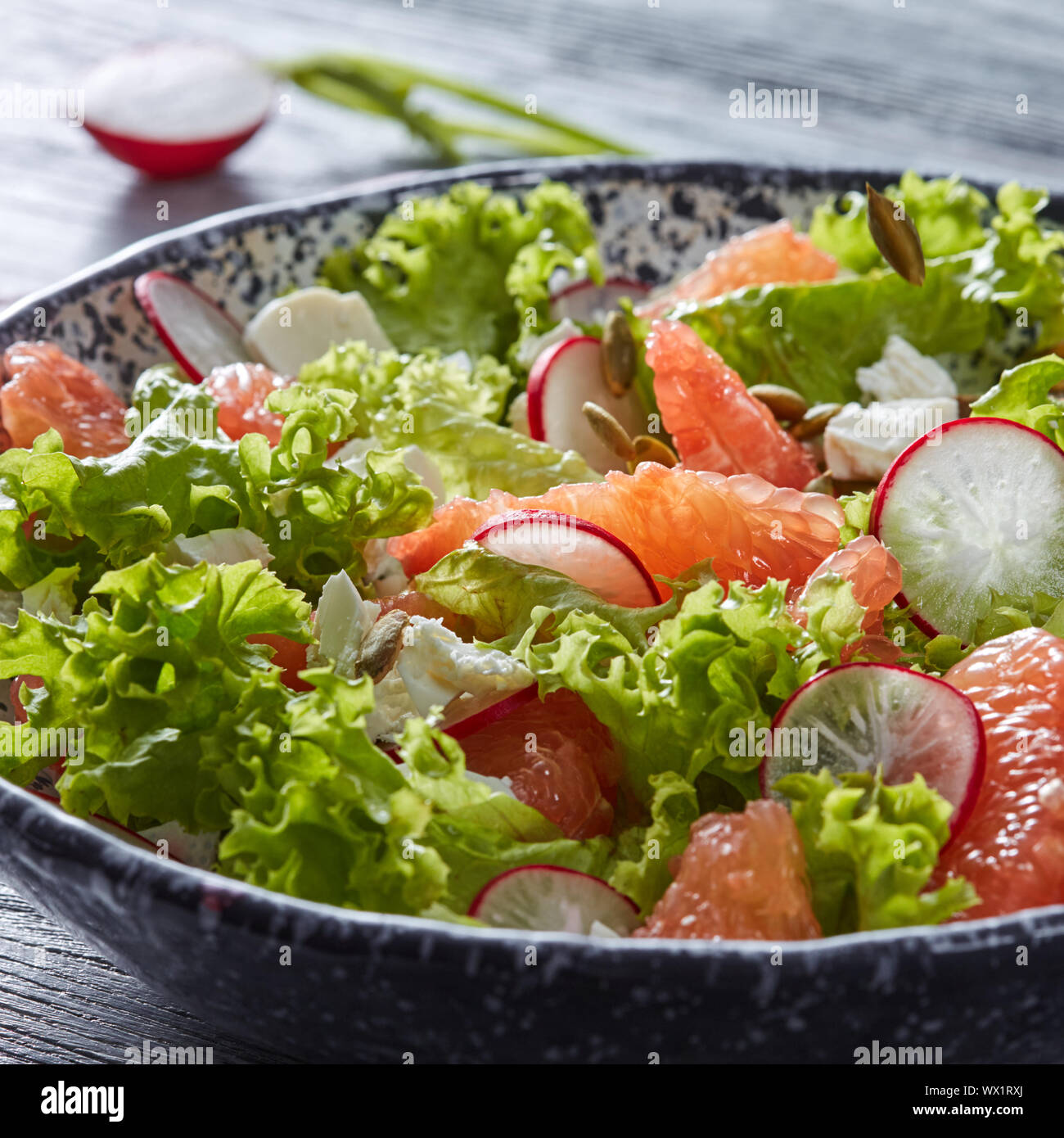 Freshly prepared dietary vegetarian salad with natural organic vegetables, citrus fruits, in a black plate on a gray wooden tabl Stock Photo