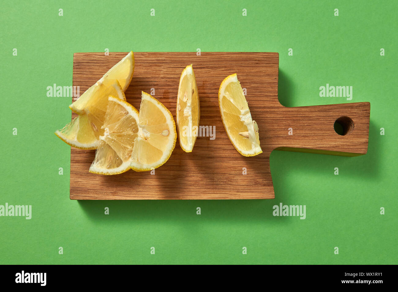 Slices of juicy ripe natural yellow lemon on a wooden board on a green background. Top view. Stock Photo