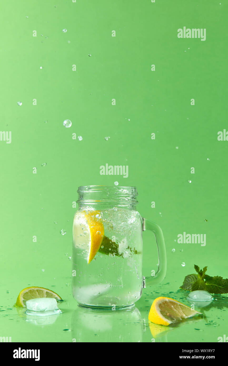 Splash lemonade in different directions from a mason jar with natural lemonade handmade. Drops of liquid and pieces of lemon and Stock Photo