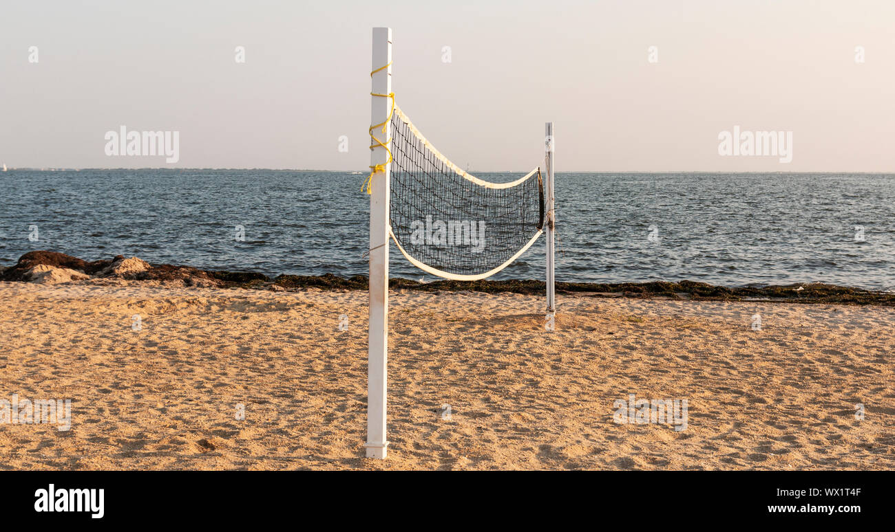 A beach has a volleyball net set up on the sand ready for athletes to