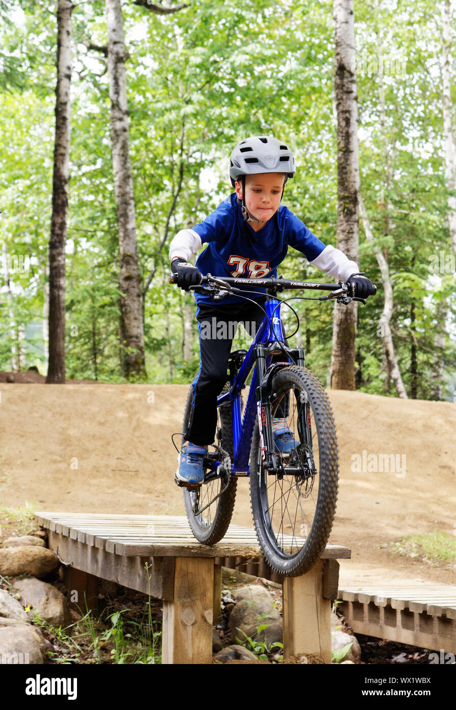 A seven year old boy on his mountain bike practicing drop-offs in a skills park Stock Photo