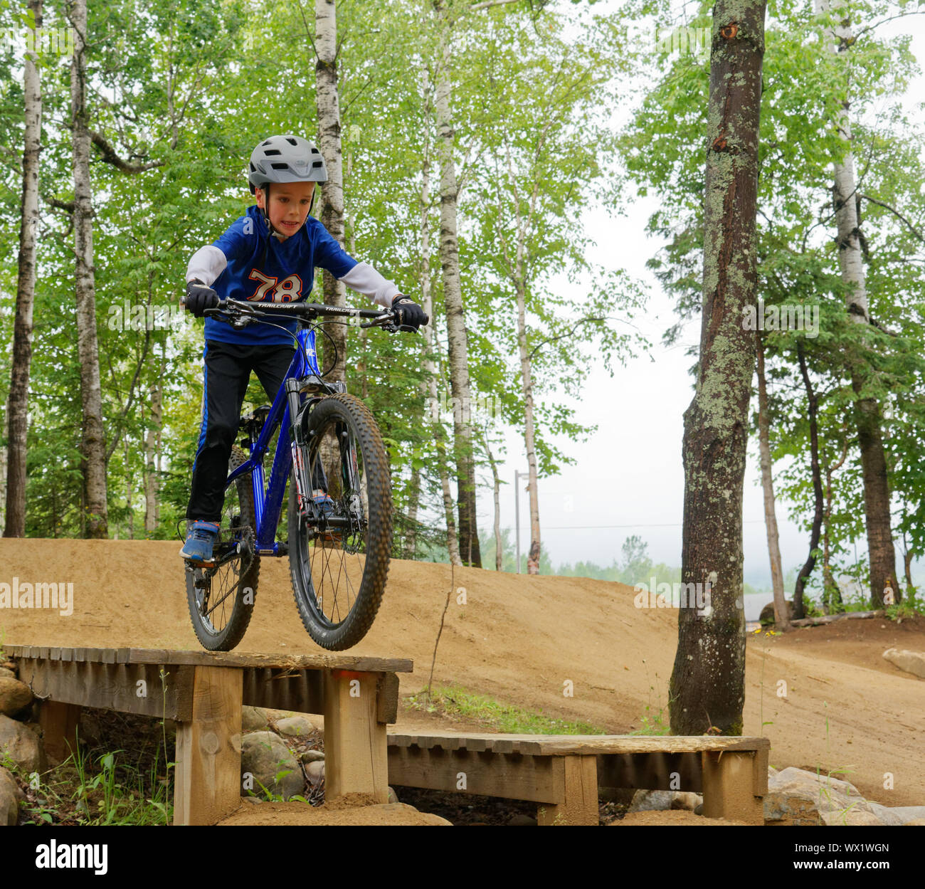 A seven year old boy on his mountain bike practicing drop-offs in a skills park Stock Photo