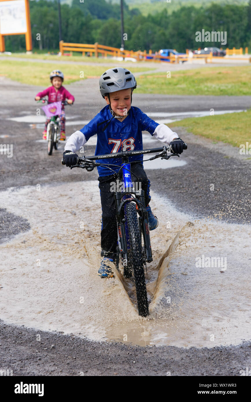 A young boy (7 yr old) riding his bike through a puddle Stock Photo