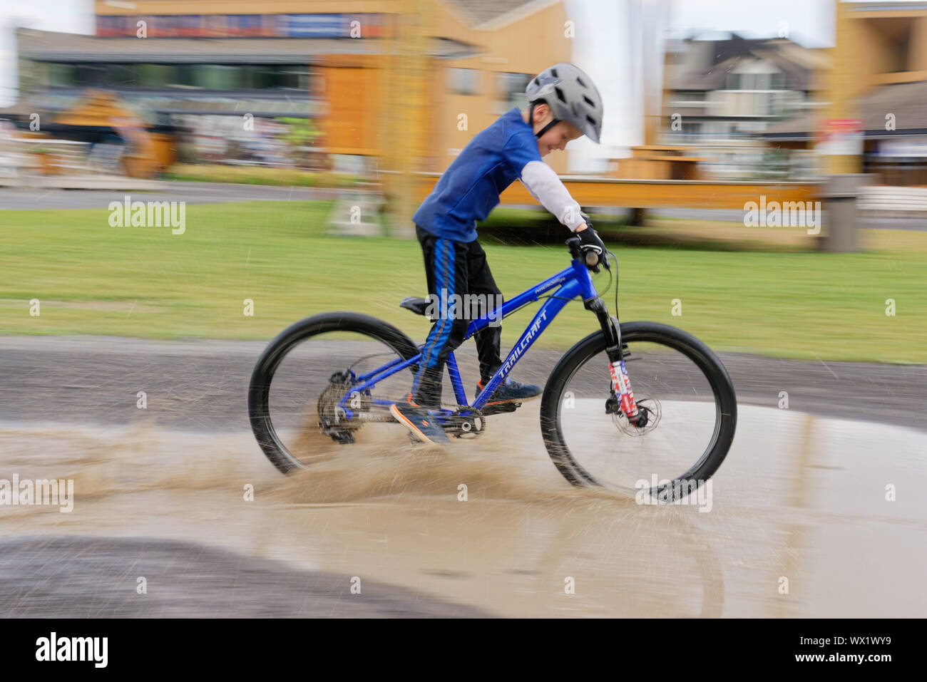 A young boy (7 yr old) riding his bike through a puddle Stock Photo