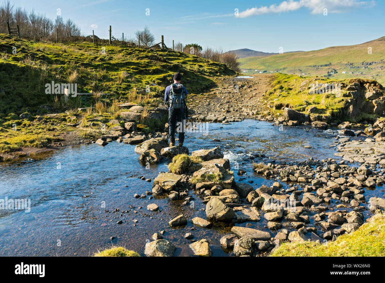 A walker using stepping stones to cross the Lon an t-Stratha stream in Glen Uig, Trotternish, Isle of Skye, Scotland, UK Stock Photo