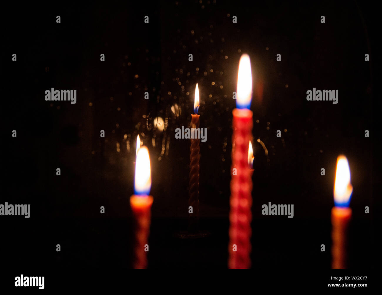 In the foreground unfocused three burning candles.They are reflected in the window glass, Stock Photo
