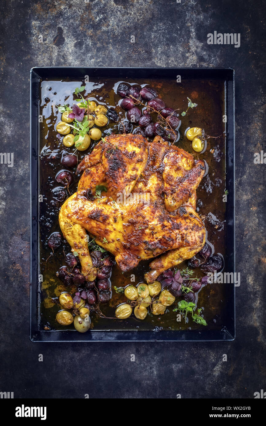 Modern spatchcocked barbecue chicken al mattone chili with red and green grapes as top view on an old metal sheet with copy spac Stock Photo