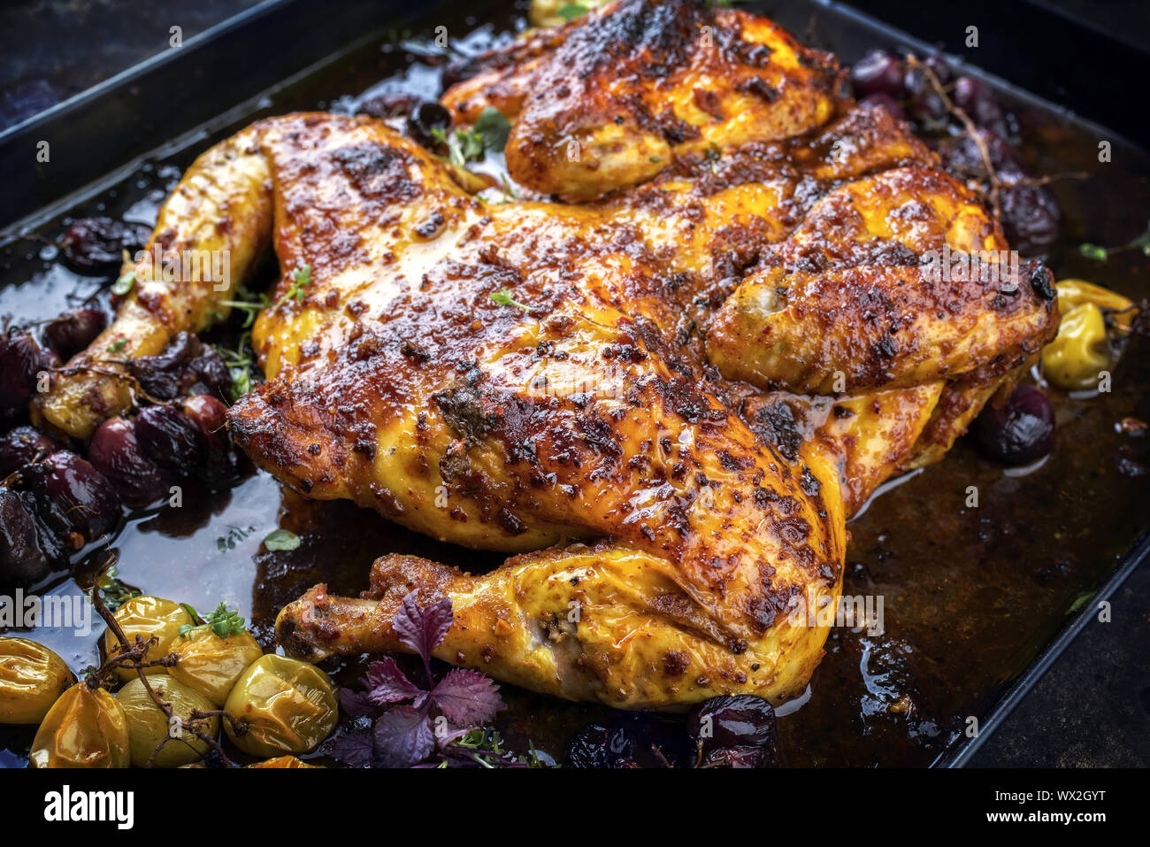 Modern spatchcocked barbecue chicken al mattone chili with red and green grapes as top view on an old metal sheet Stock Photo
