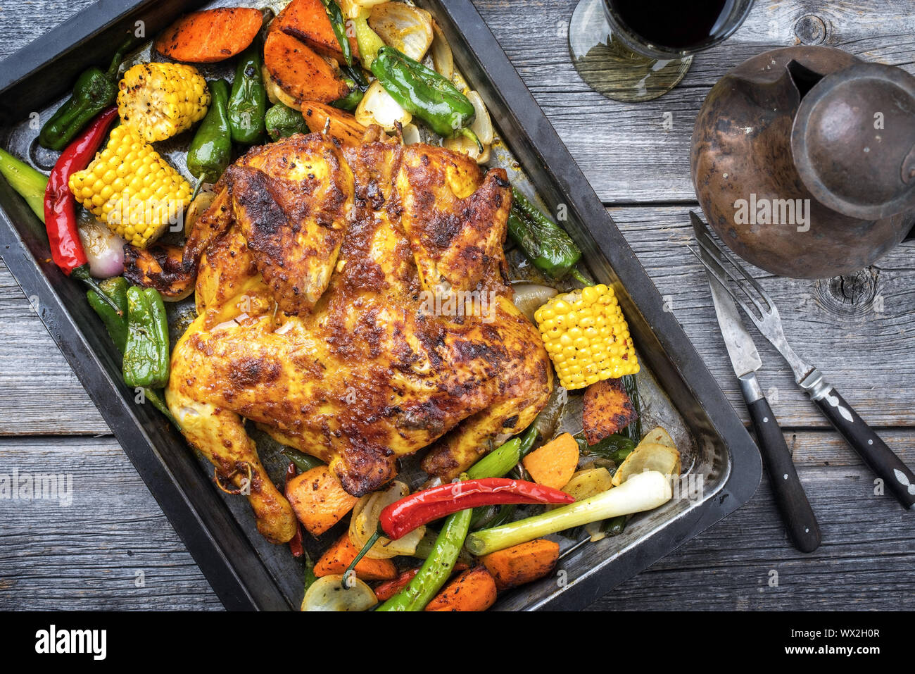 Spatchcocked barbecue chicken al mattone chili with corn and vegetable as top view on an old metal sheet Stock Photo