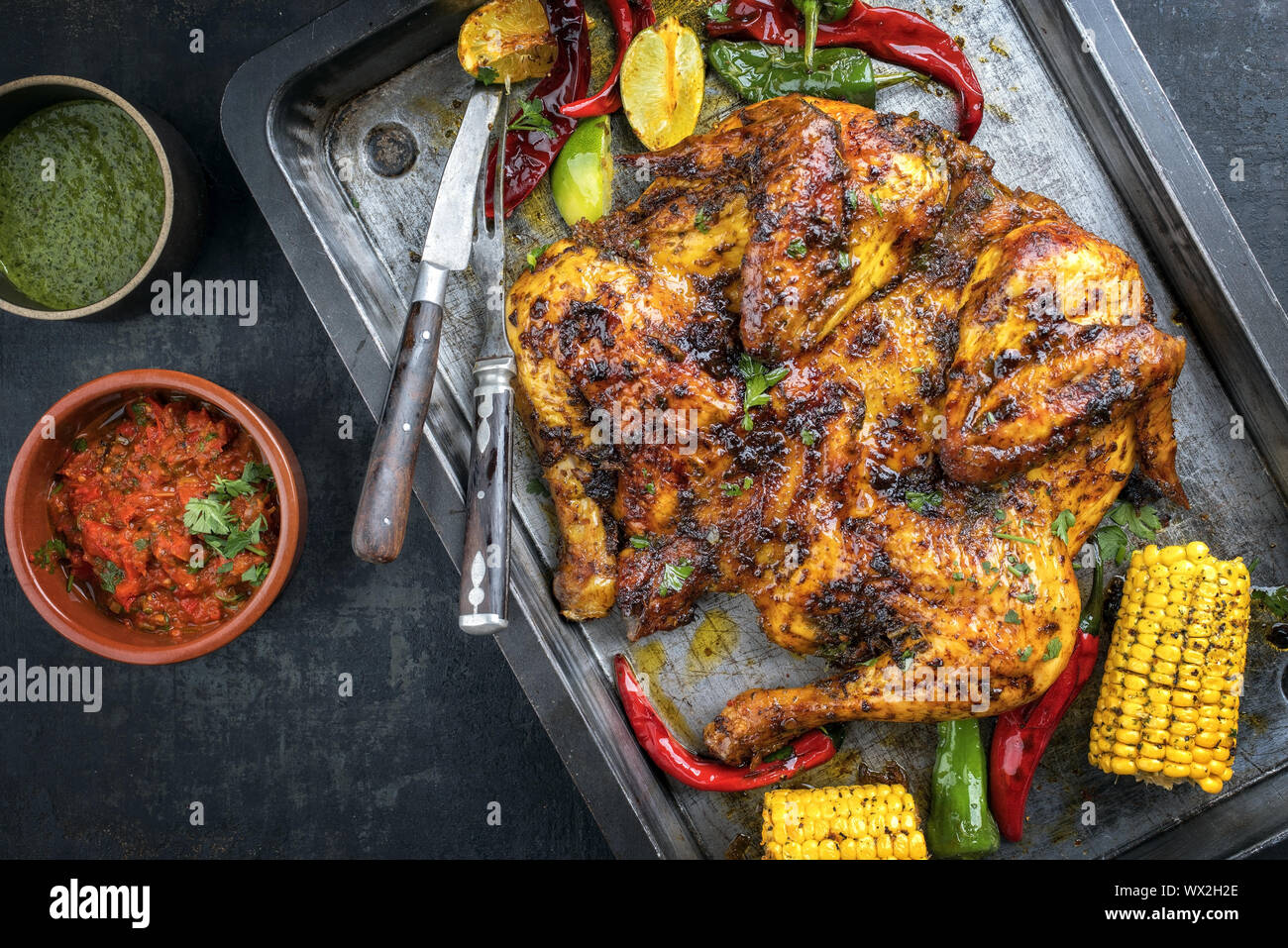 Spatchcocked barbecue chicken al mattone chili with chimichurri sauce and chili relish as top view on an old metal sheet Stock Photo