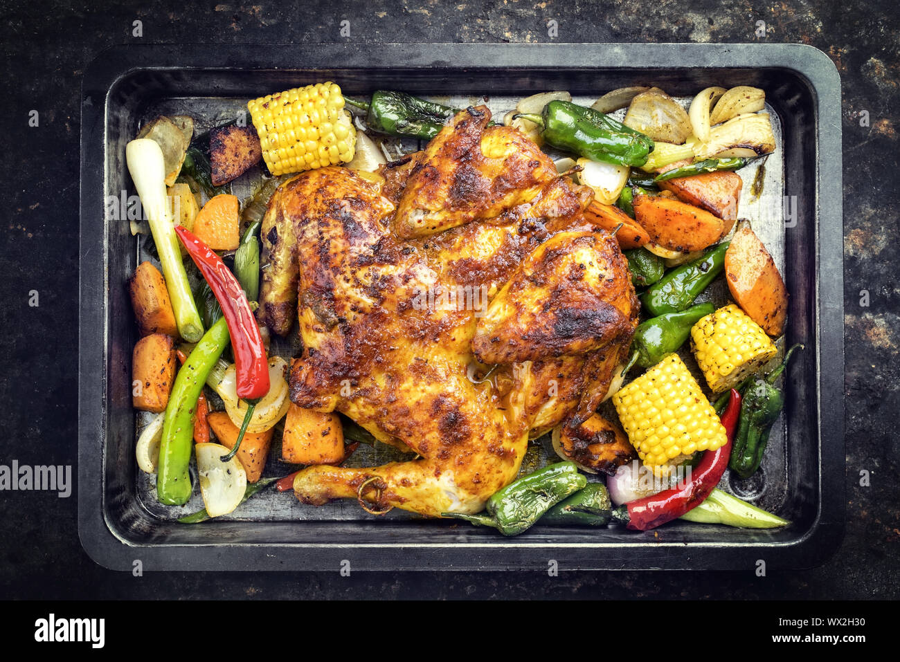 Spatchcocked barbecue chicken al mattone chili with corn and vegetable as top view on an old metal sheet Stock Photo