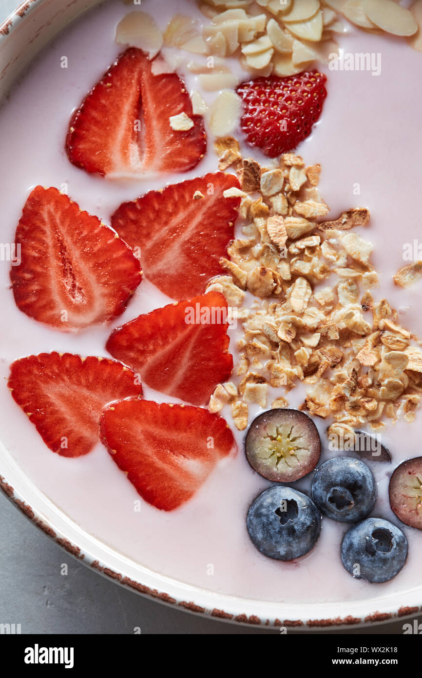 Homemade granola in a plate, sliced strawberries, yogurt, almonds, blueberries - ingredients for natural breakfast on a gray tab Stock Photo