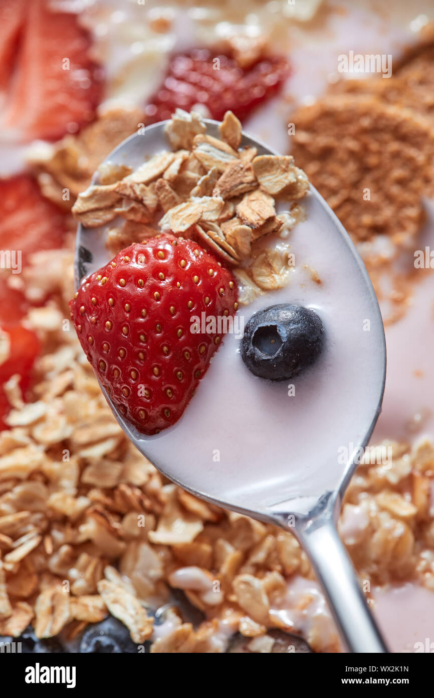 Close-up of spoon with fresh natural homemade morning breakfast with strawberries, milk dessert, oat cereal, blueberries above t Stock Photo