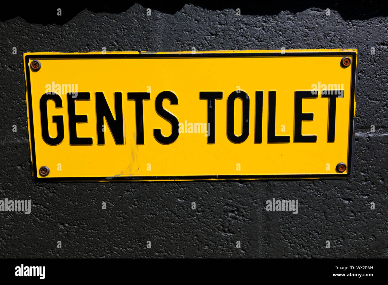 Yellow gents toilet sign on black painted wall. Stock Photo