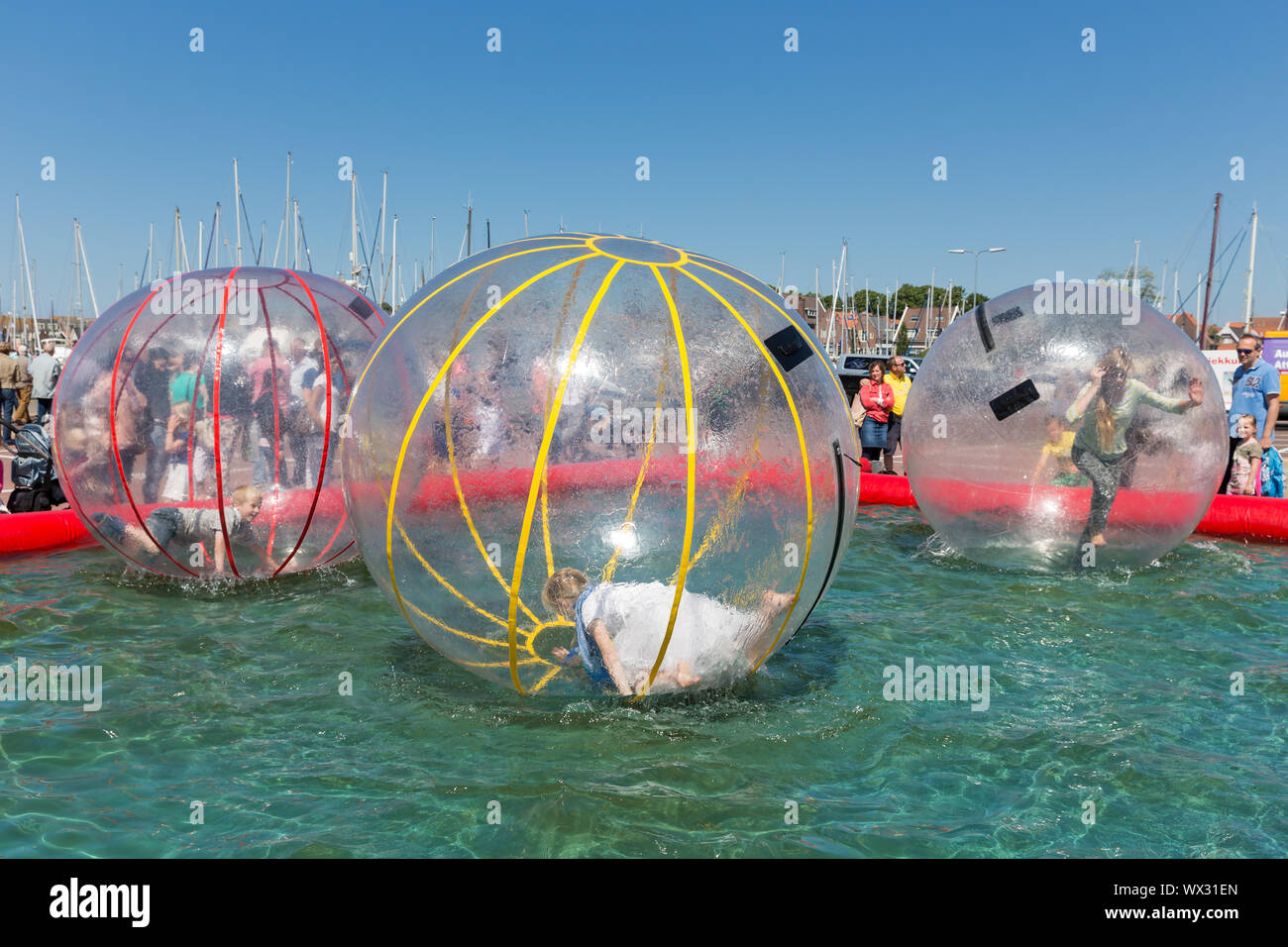 Children have fun inside plastic balloons on the water during a fishing fare Stock Photo