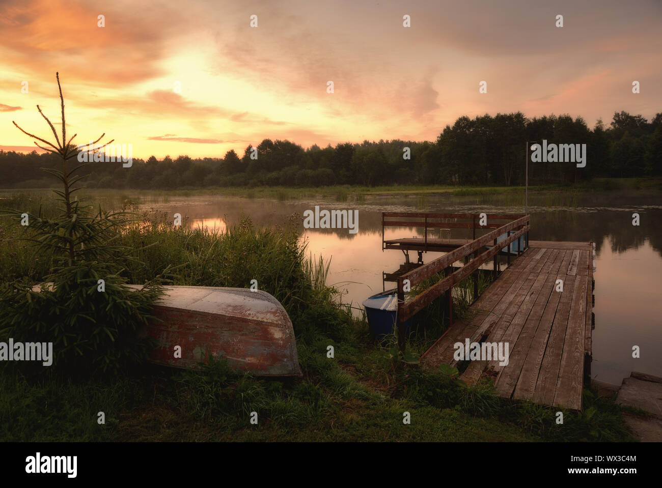 Summer sunset on a forested river with inverted boats and a old wooden pier Stock Photo