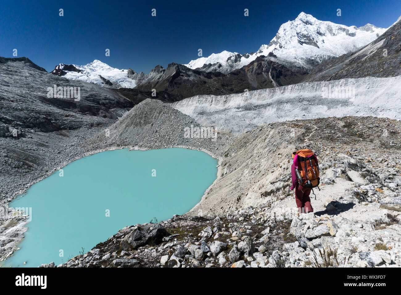 female mountain climber passes by a turquoise lake in the Andes in Peru Stock Photo