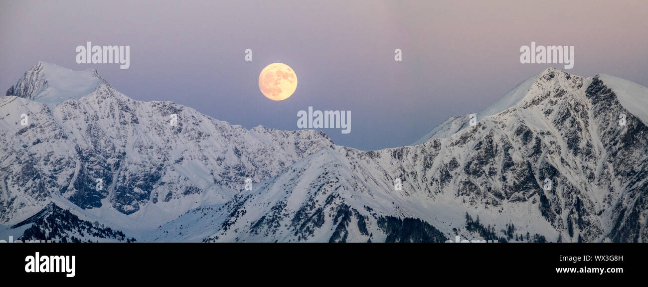 full moon rising into a night sky in a winter mountain landscape Stock Photo