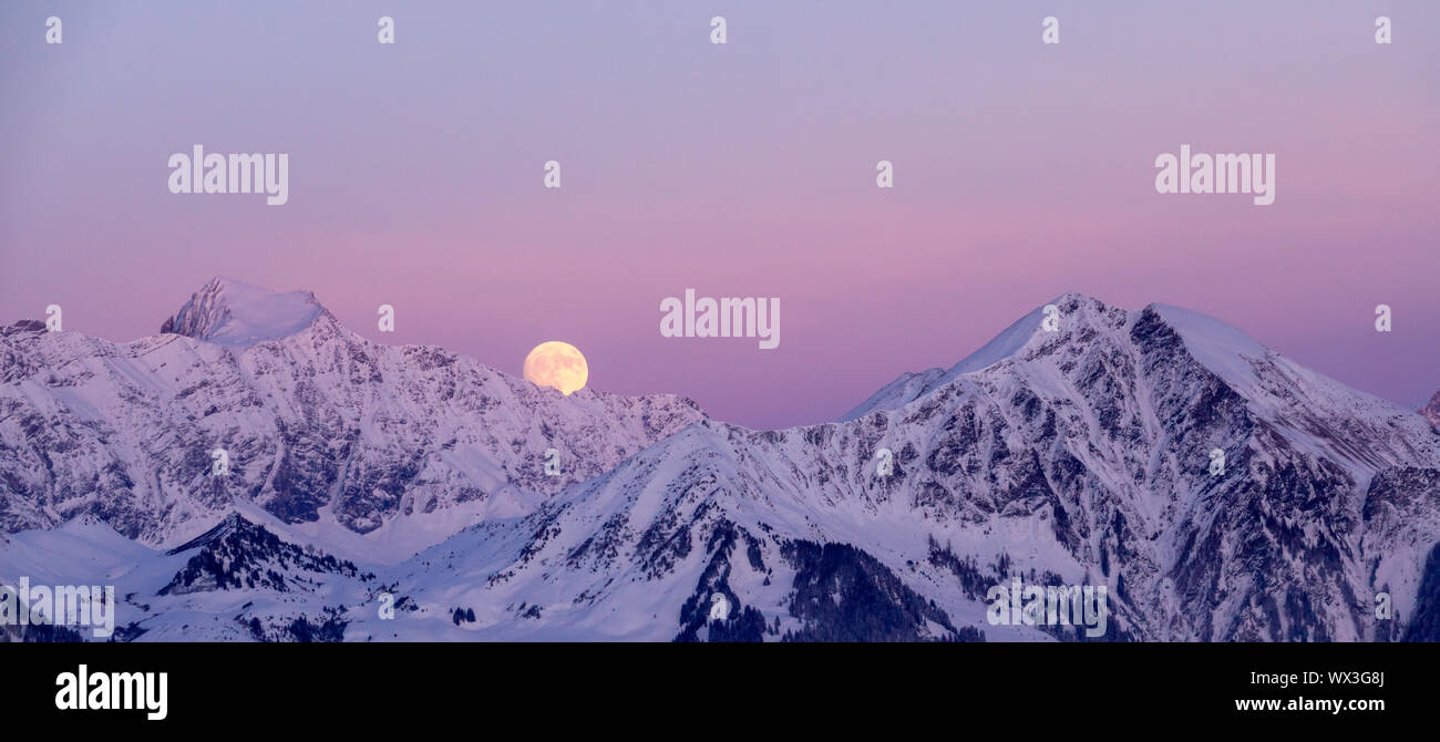 full moon rising into a pink sky in a winter mountain landscape Stock Photo