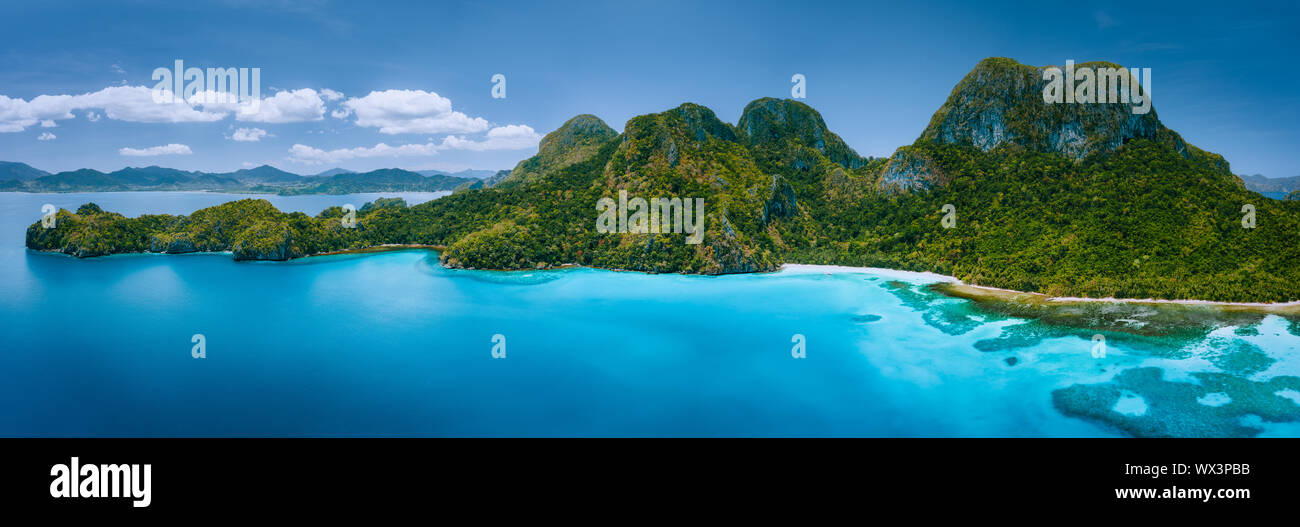 Aerial drone panoramic view of uninhabited tropical island with rugged mountains, rainforest jungle, sandy beaches surrounded by blue ocean Stock Photo