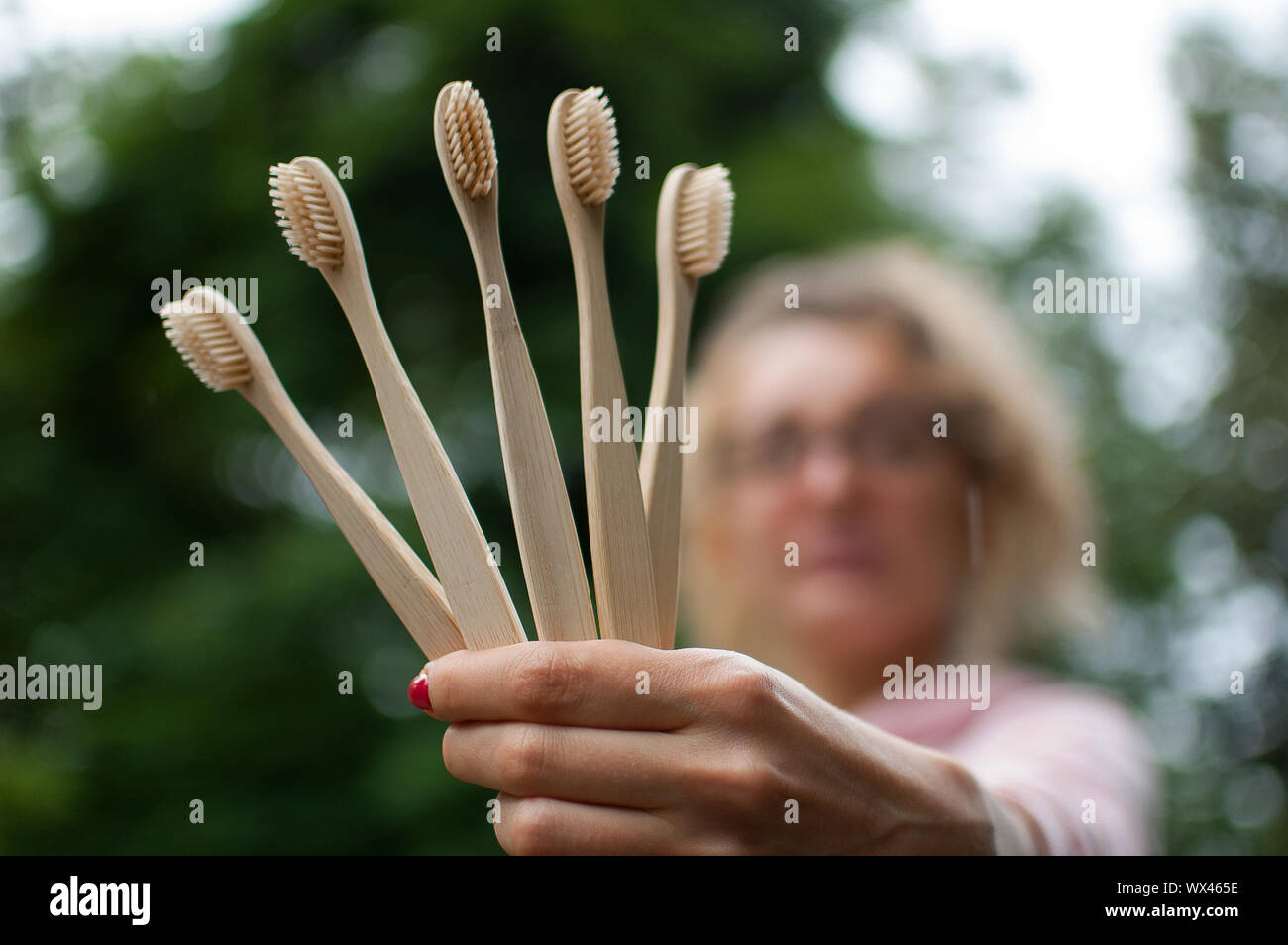 Young beautiful woman with blonde curly hair in pink hipster jacket and eyeglasses holding five bamboo toothbrushes in hand. Zero waste concept Stock Photo