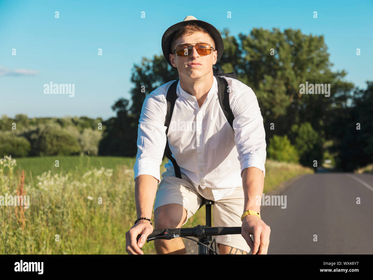 Portrait of confident young cyclist in sunglasses riding along countryside road Stock Photo