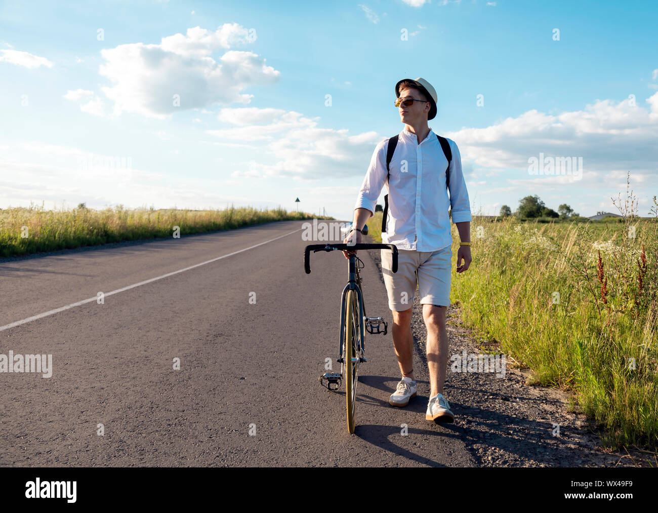 Young man walking and wheeling his bicycle along rural field road Stock Photo
