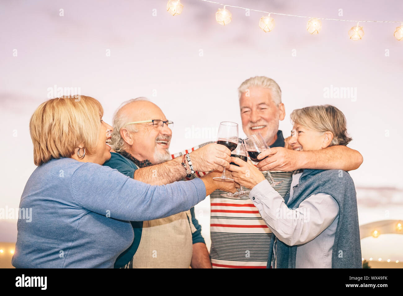 Happy senior friends cheering and toasting with red wine on terrace - Older people having fun at dinner party on patio at sunset Stock Photo