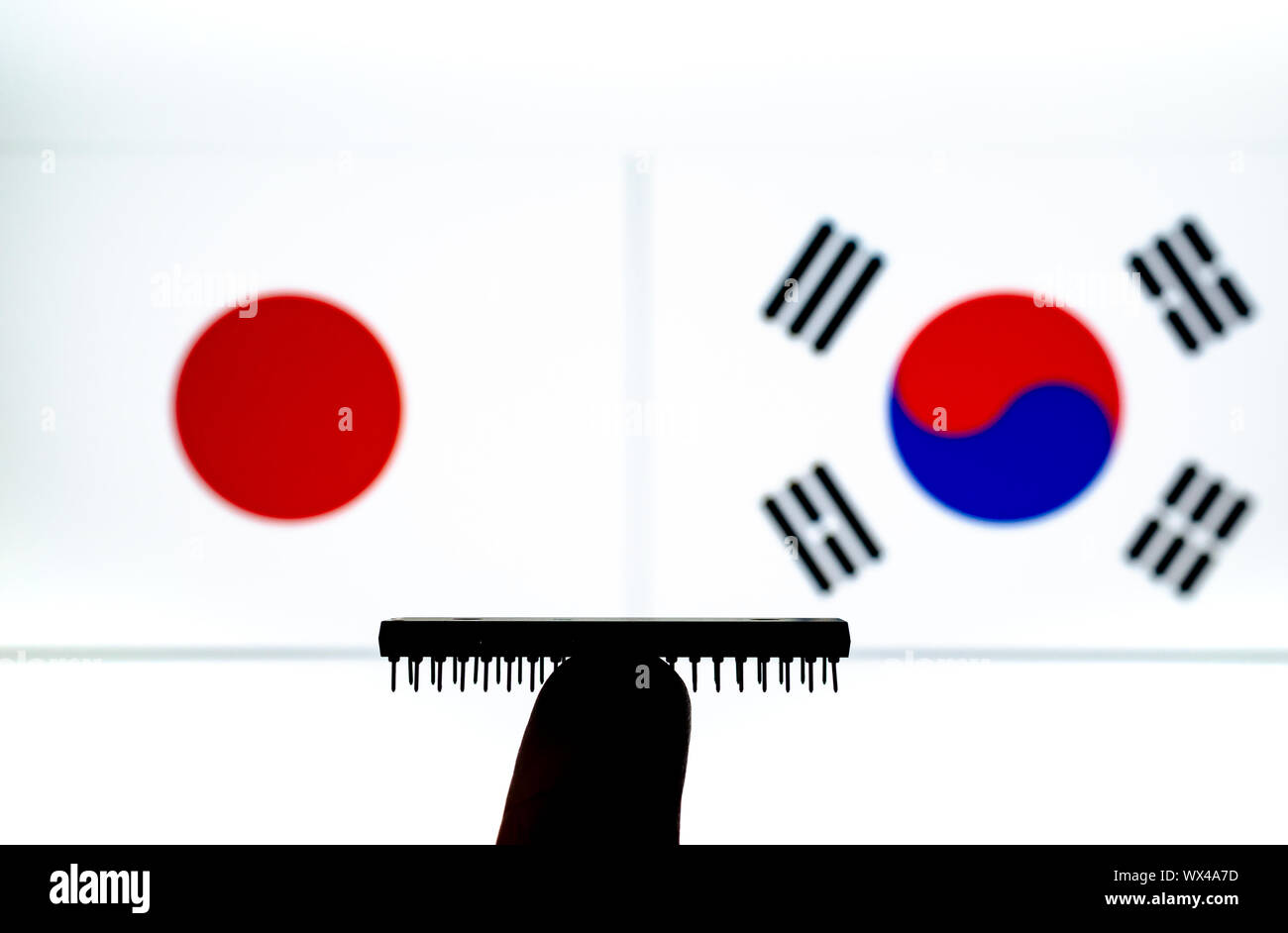 Silhouette of a semiconductor chip balancing on the finger and flags of Japan and South Korea on a blurred screen. Conceptual photo for trade talks. Stock Photo