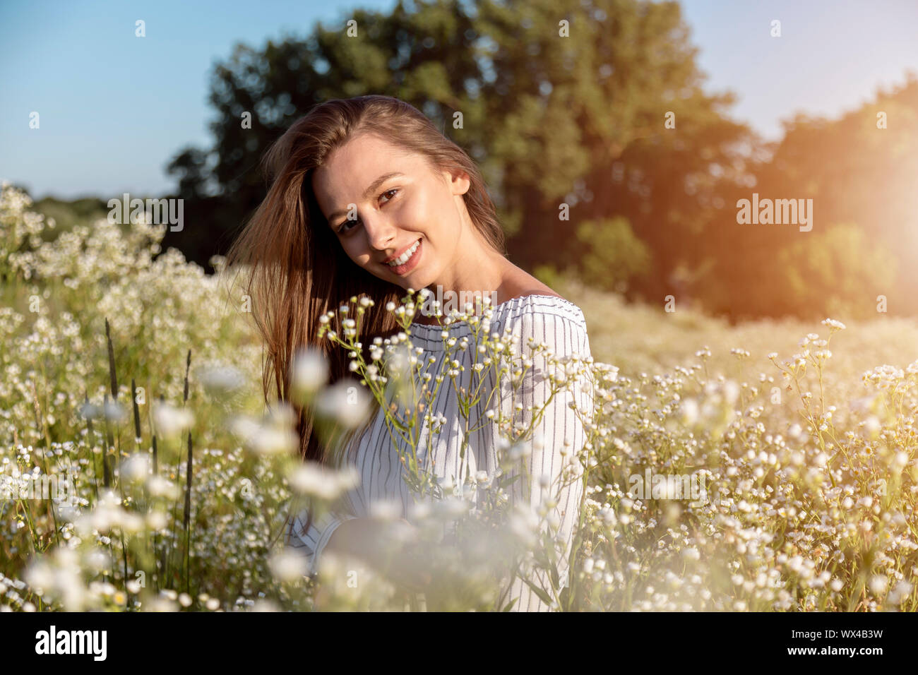 Cheerful young brown-haired beauty posing on a flowery forest edge Stock Photo