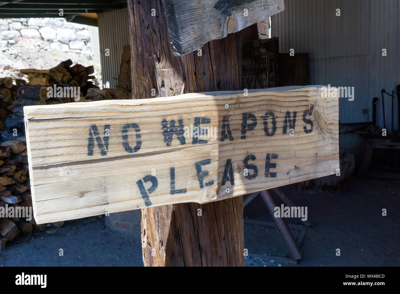 rusti wooden baord sign on a post with the warning no weapons written as instructions before enter Stock Photo
