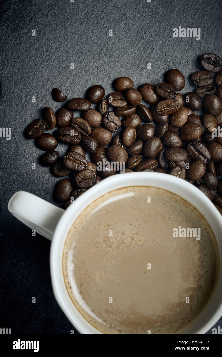 Top view of hot coffee latte in a white cup with roasted arabica coffee beans on slate background Stock Photo