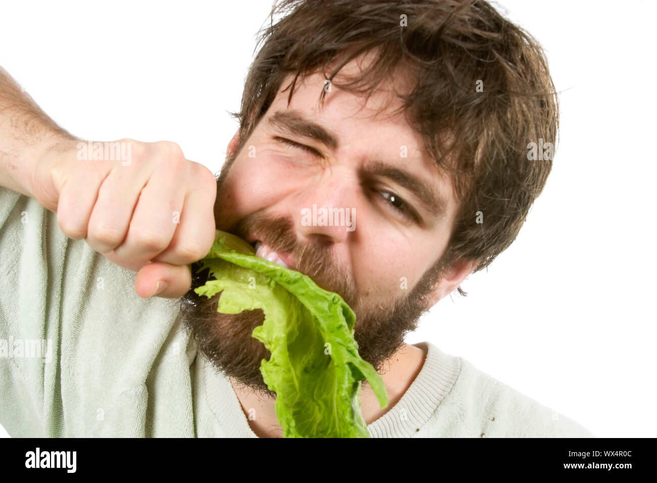 A young male with a beard is eagerly eating salad, as if he were a barbarian eating meat. Stock Photo