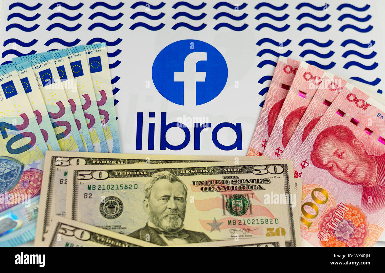 Facebook and Libra logos on the brochure surrounded by US Dollars, Euros and Chinese Renminbi banknotes. Conceptual photo. Stock Photo