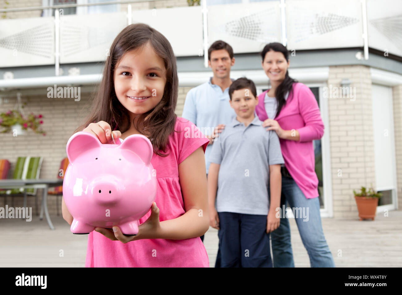 Beautiful little girl inserting coin in a piggy bank with her family in ...