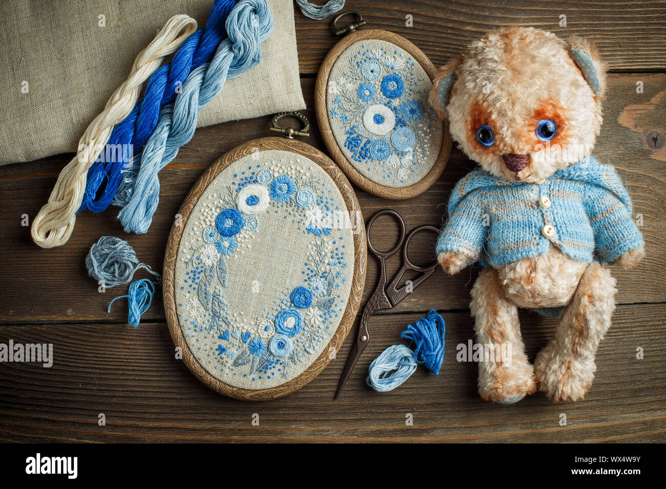 Two embroideries in decorative frames, accessories for embroidery, and Teddy bear's toy on wooden background Stock Photo