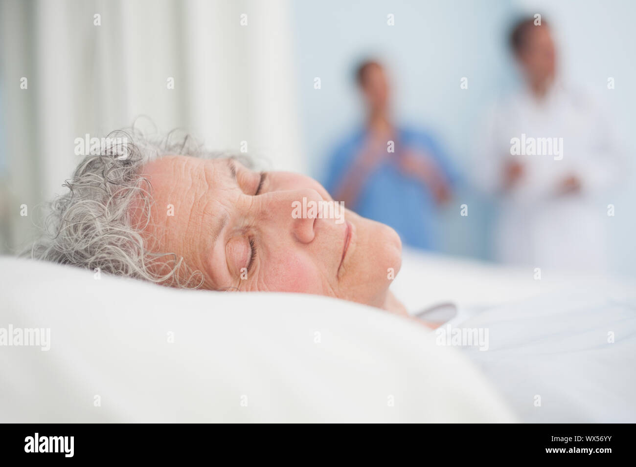 Elderly patient sleeping on a bed next to a doctor in hospital ward