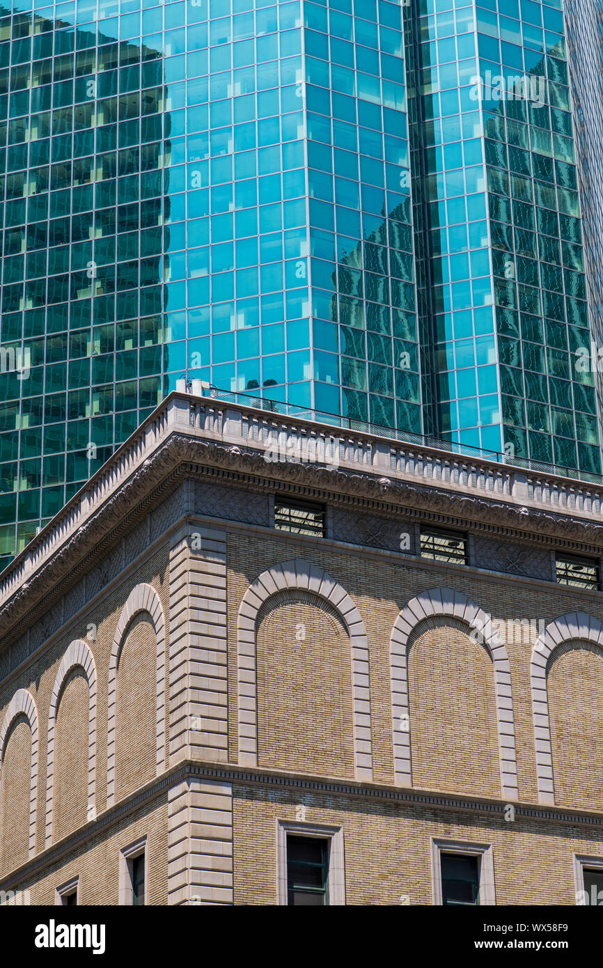 Modern glass and steel skyscraper contrasted with an old brick building with ornate trim and arches in New York City Stock Photo