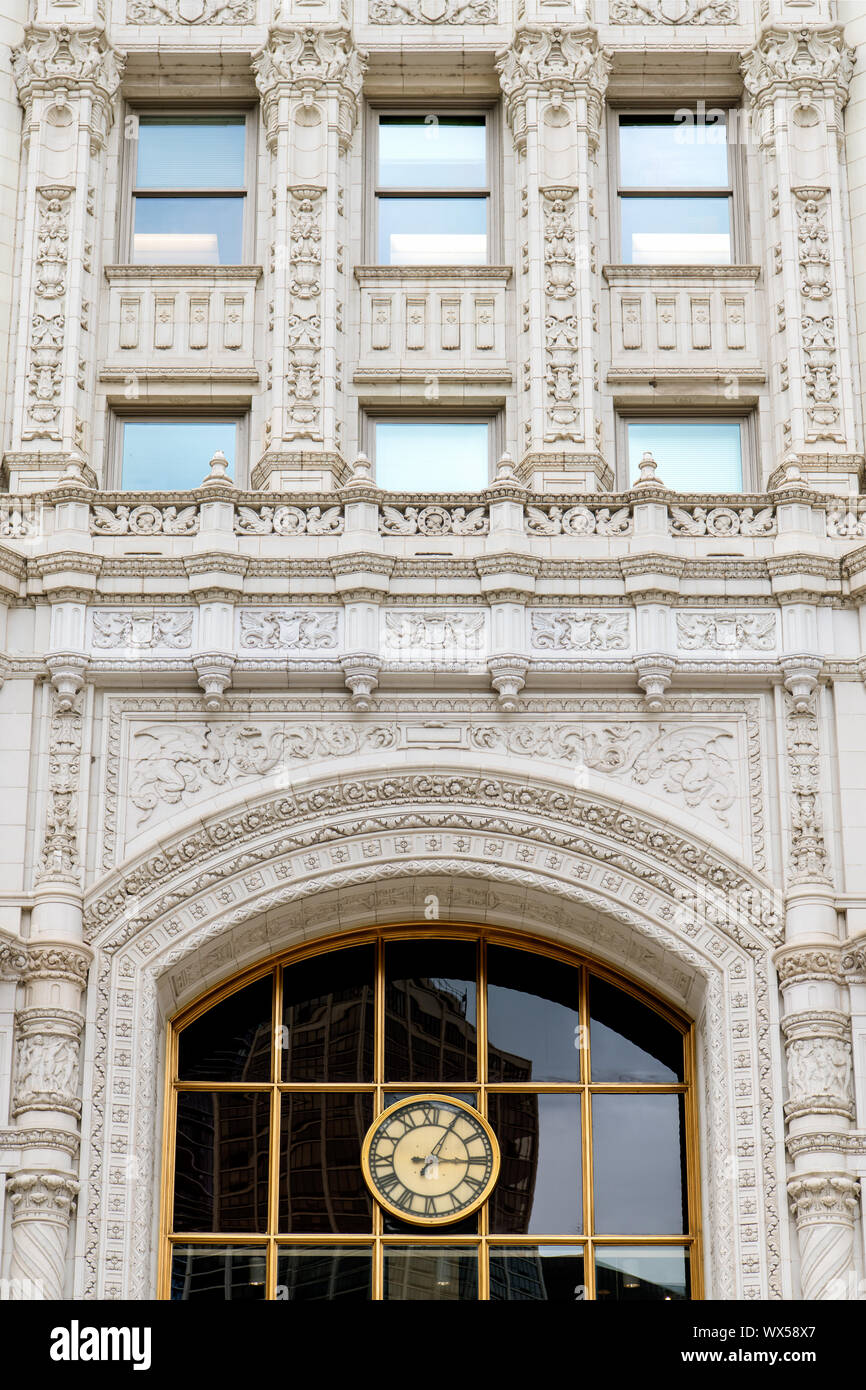 Ornate white facade of an historic building with a clock with Roman numerals and a large window reflecting modern office buildings in downtown Chicago Stock Photo