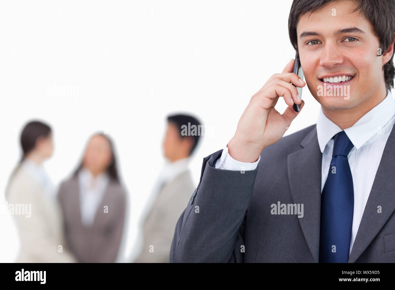 Smiling salesman on his cellphone with team behind him against a white ...