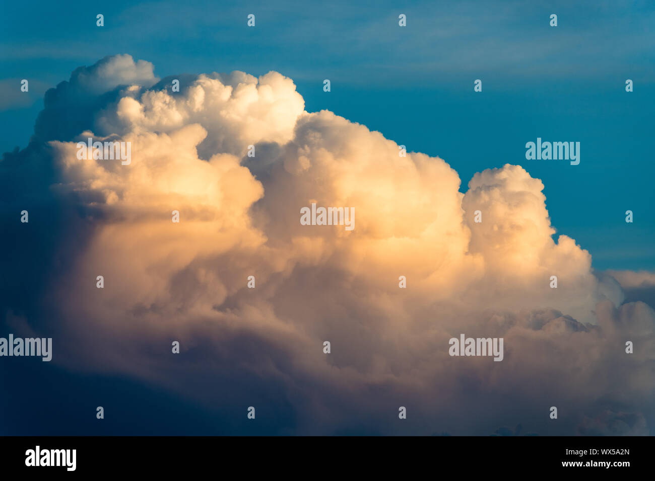 Cloudscape of dramatic white fluffy cumulus clouds illuminated by evening light contrasted with blue sky Stock Photo