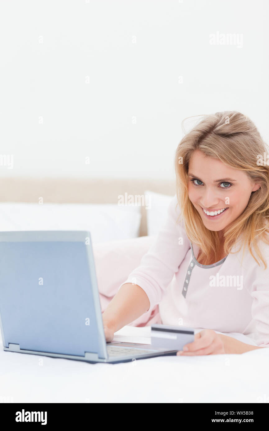 A smiling woman lying on her bed as she uses her laptop while looking ...