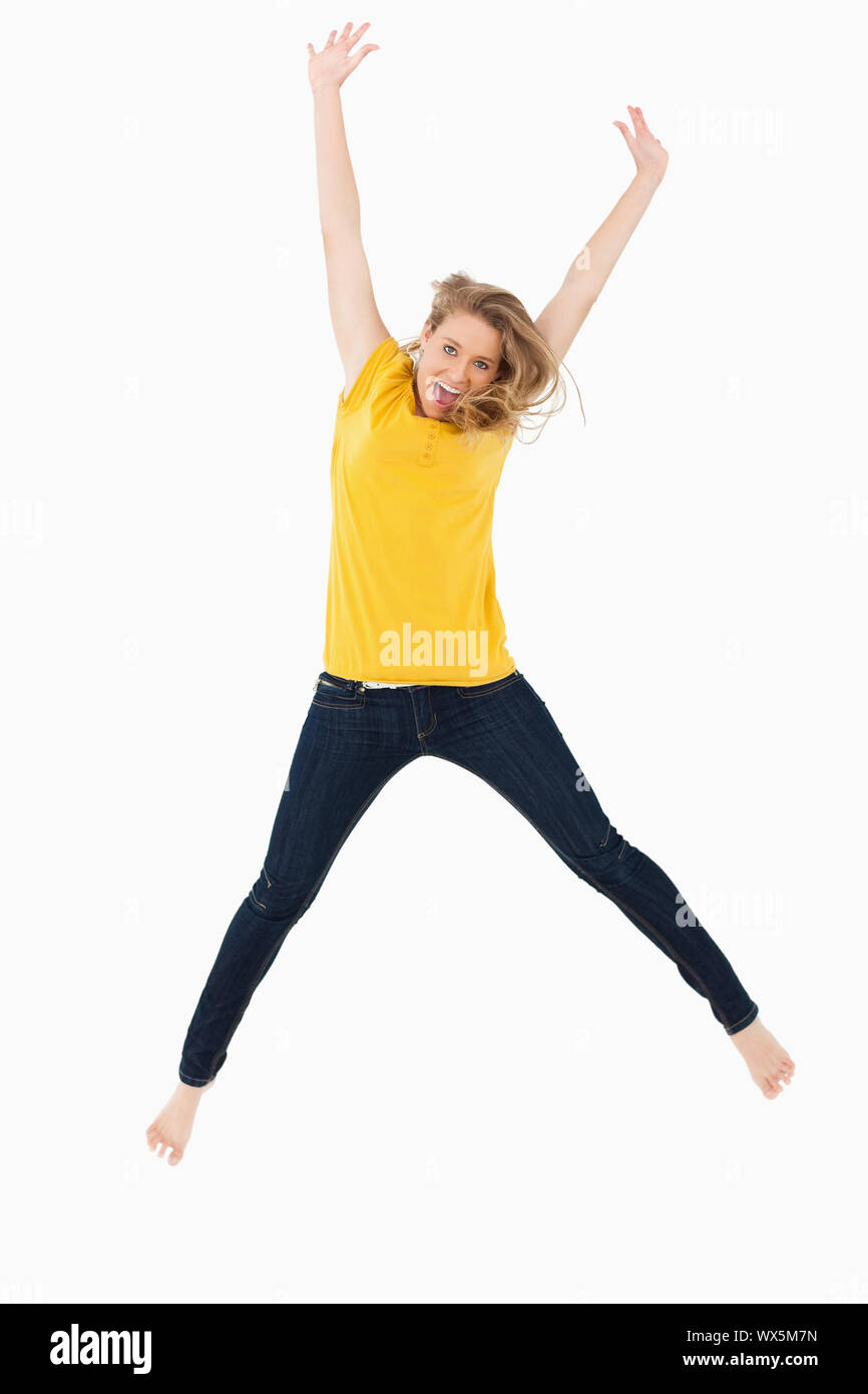 Young blonde woman in yellow shirt jumping against white background ...